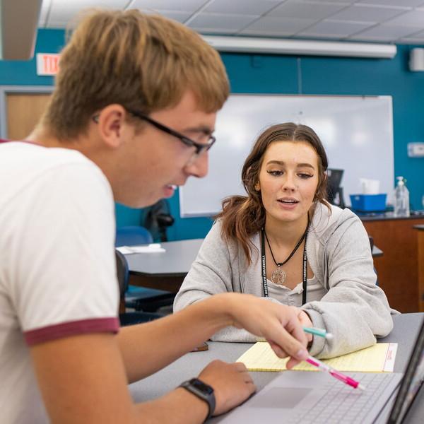 A female and male student seated at a table looking at a laptop screen.