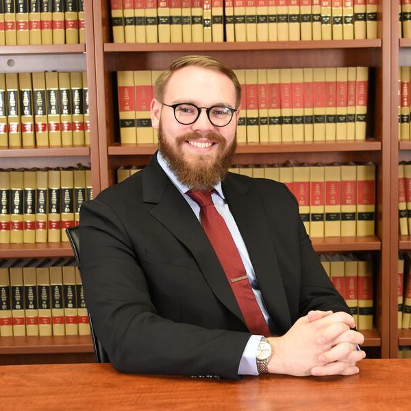 Adam Braegelman sitting with his hands folded on a table in front of a bookcase.