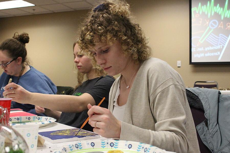 Hearing impaired student paints on a canvas with other students at a recreational event for students.