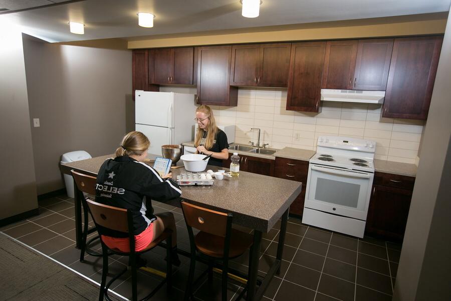 Two young women in a large kitchen talking over a countertop.