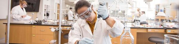 Female chemistry student conducts extracts liquid from a beaker in a lab.