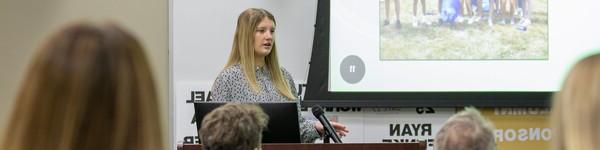 Student gives a presentation with a slide projected on a screen in front of an audience.