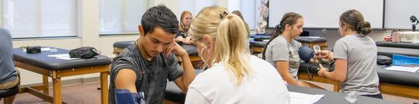 Athletic training students paired of taking blood pressure in a classroom lab. 