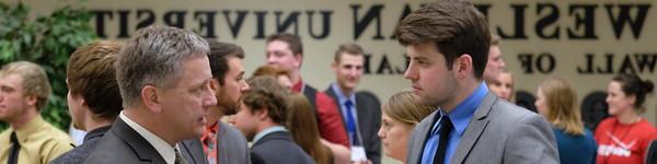 In a crowded Great Hall dressed in a suits, a male student talks with an adult male.