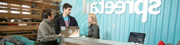 Standing a the Spreetail reception desk talking are three adults.