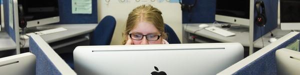 Female student looking at a large monitor surrounded by cubicles with large monitors.