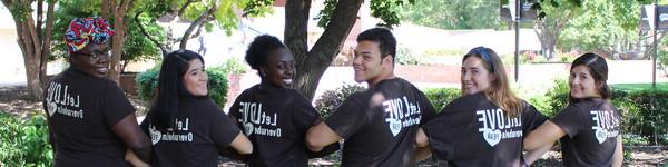 Arm in arm, students look over their shoulder with t-shirts that say Let Love Overwhelm Fear.