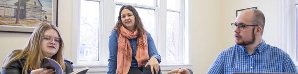 英语 professor Mary Hickman sits between two students as they discuss a book.